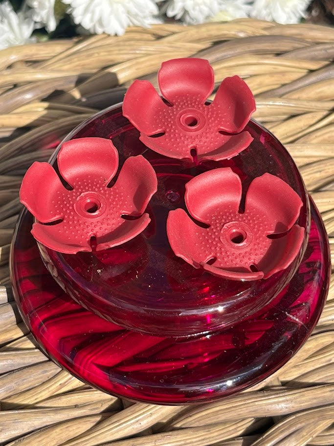 Red flower-shaped hummingbird feeder with white flowers in the background