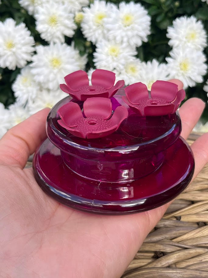 Red flower-shaped hummingbird feeder held in a hand with white flowers in the background