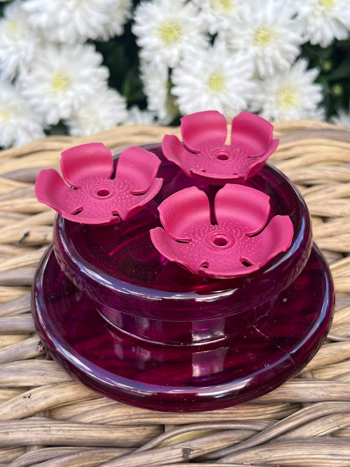 Red flower-shaped hummingbird feeder  with white flowers in the background