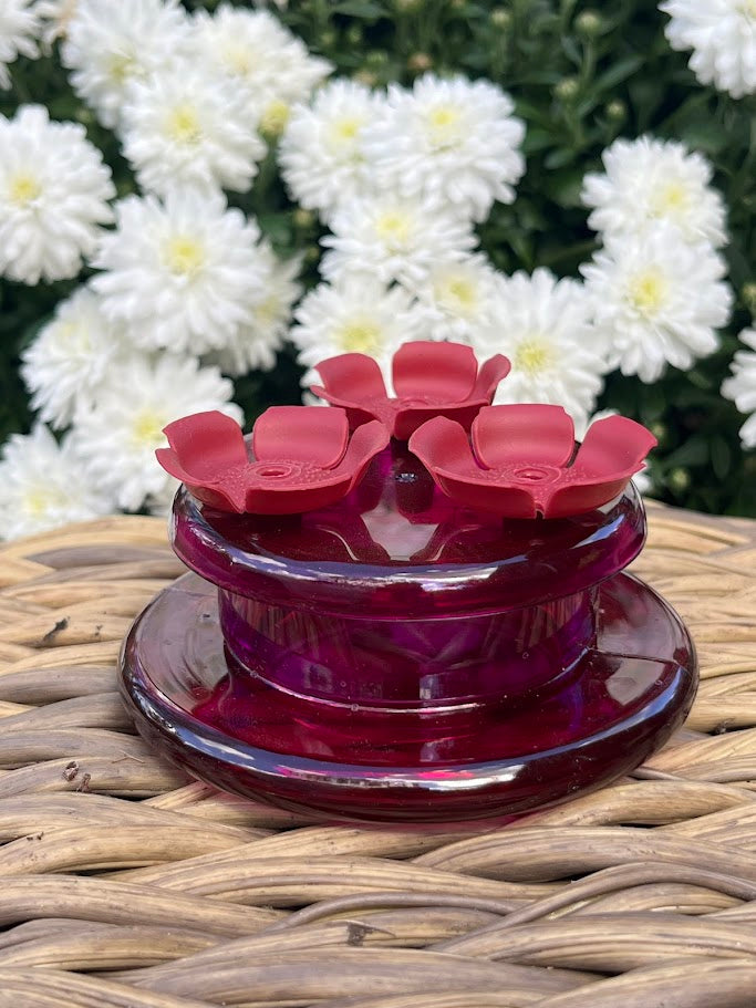 Red flower-shaped hummingbird feeder  with white flowers in the background