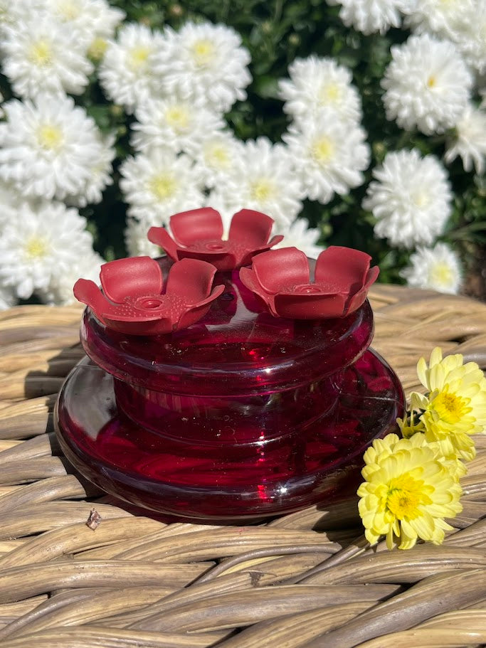 Red flower-shaped hummingbird feeder with white flowers in the background