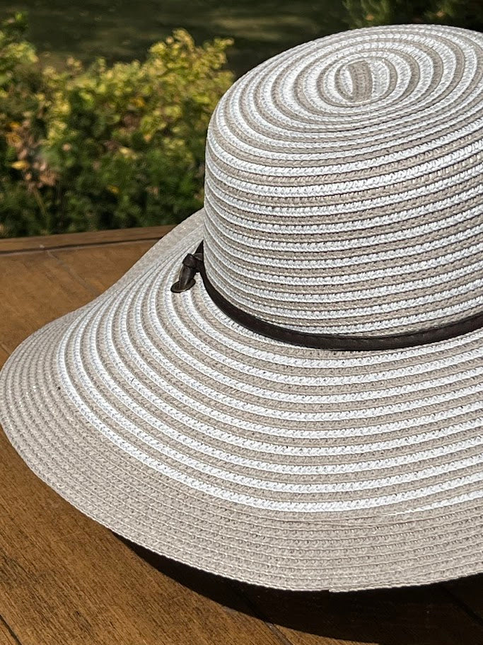 White straw sun hat with a black band on a wooden surface with blurred greenery in the background