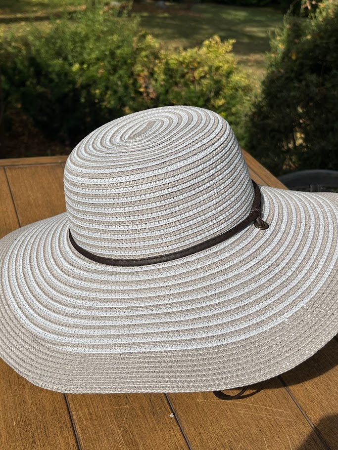White straw hat with a wide brim on a wooden surface with greenery in the background