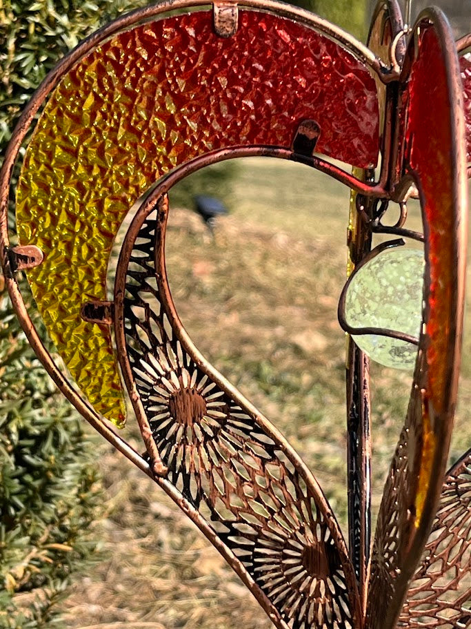 Decorative heart-shaped metal ornament hanging outdoors with greenery in the background