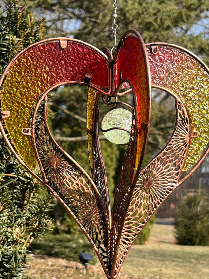Decorative heart-shaped metal ornament hanging outdoors with greenery in the background