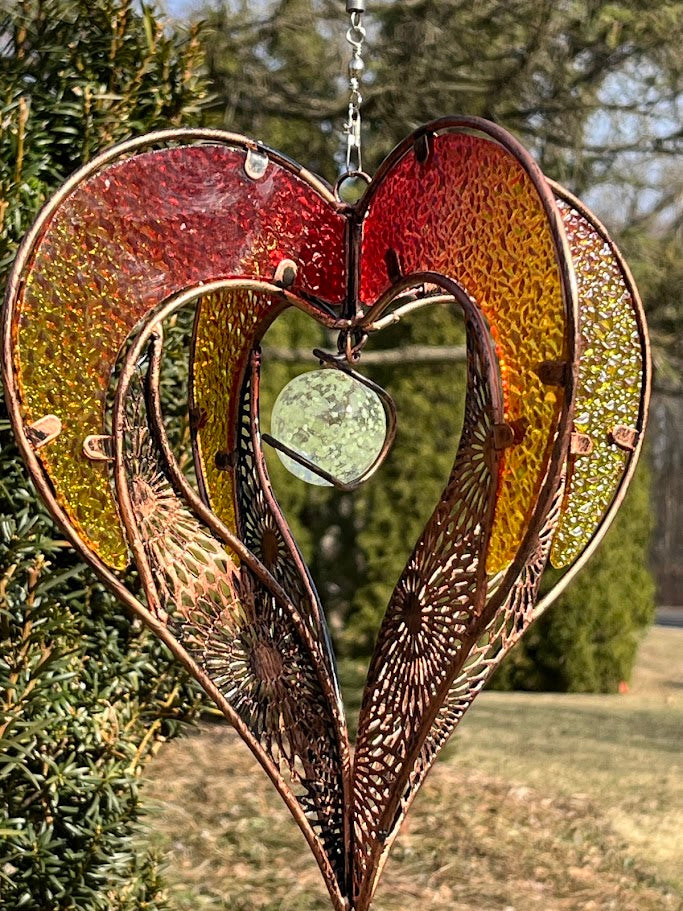 Decorative heart-shaped metal ornament hanging outdoors with greenery in the background