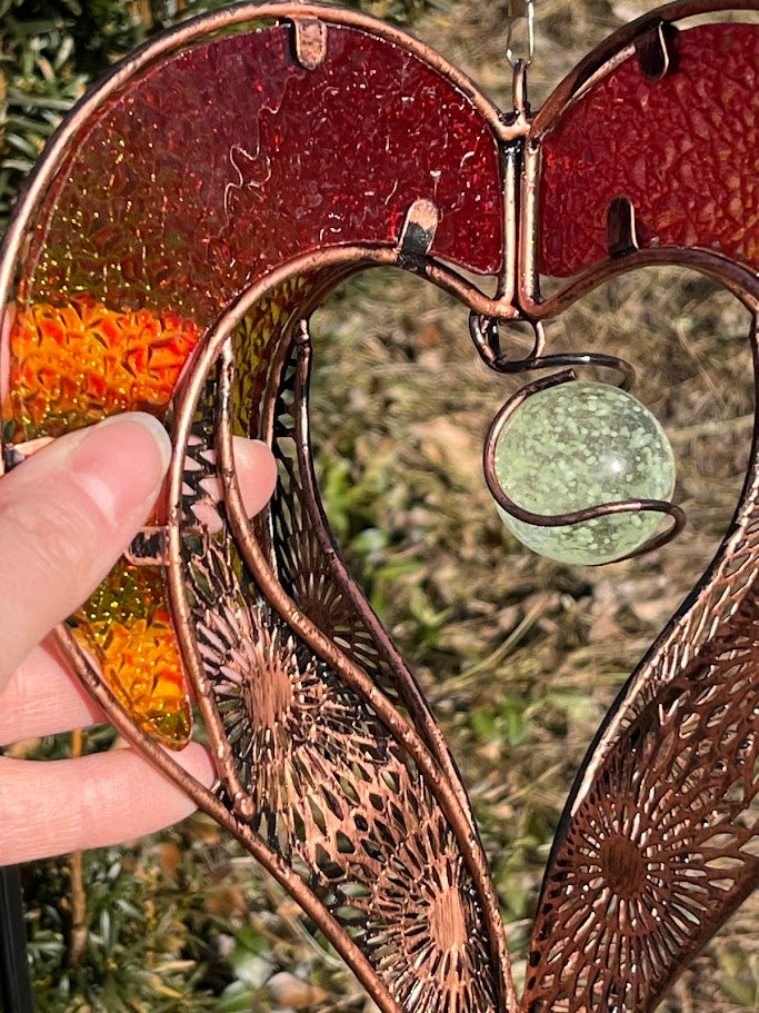 Decorative heart-shaped metal ornament hanging outdoors with greenery in the background