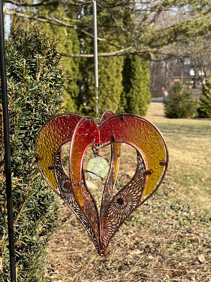 Decorative heart-shaped metal ornament hanging outdoors with greenery in the background