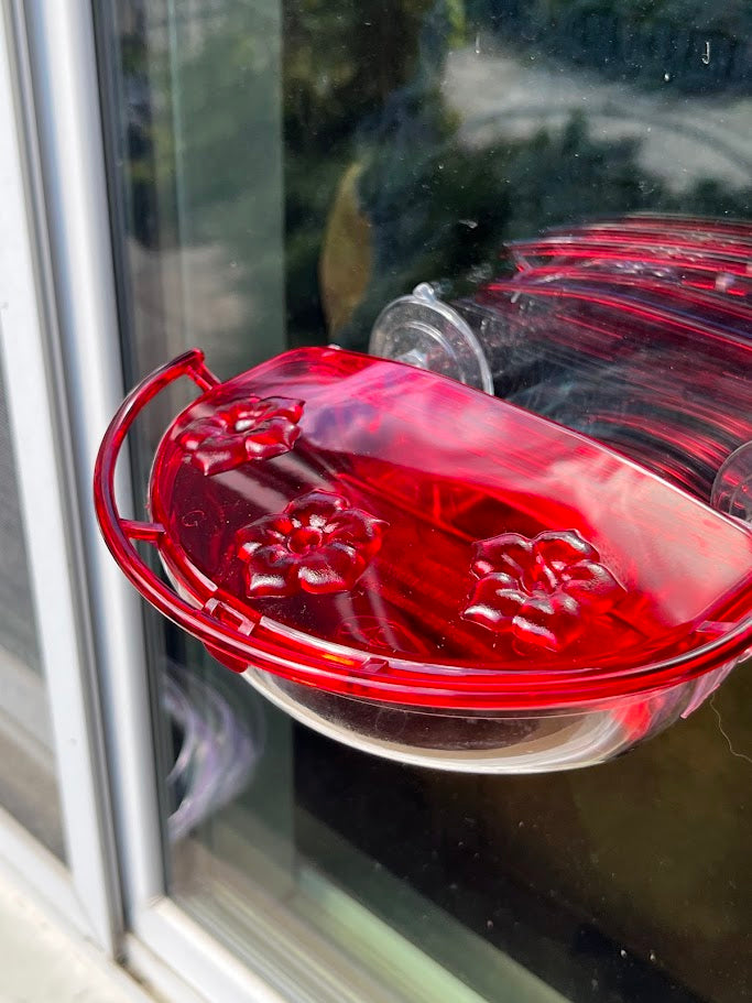 Red and clear hummingbird feeder attached to a window