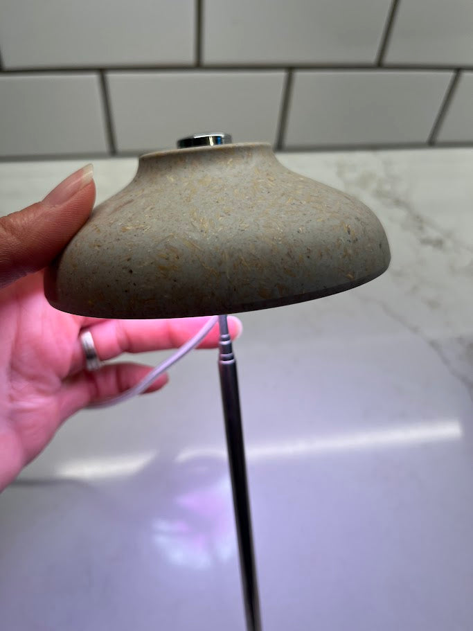 Small lamp with a white bulb inside a pot of green plants against a tiled wall.