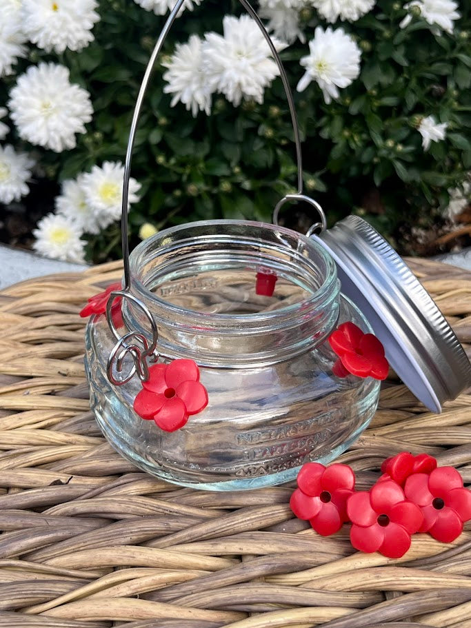 Glass mason jar hummingbird feeder on a woven surface with white flowers in the background