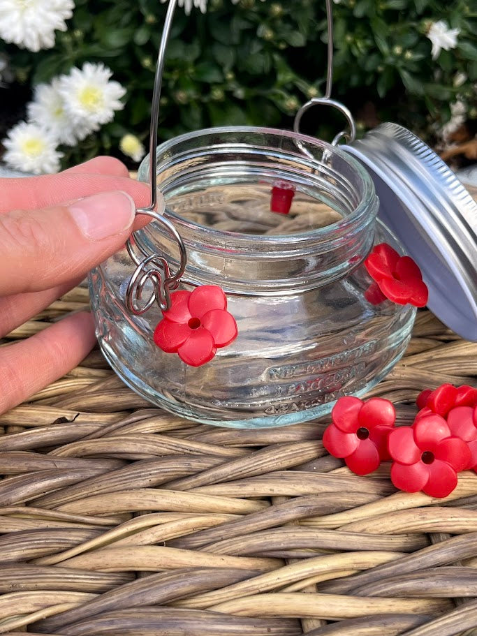 Glass mason jar hummingbird feeder on a woven surface with white flowers in the background