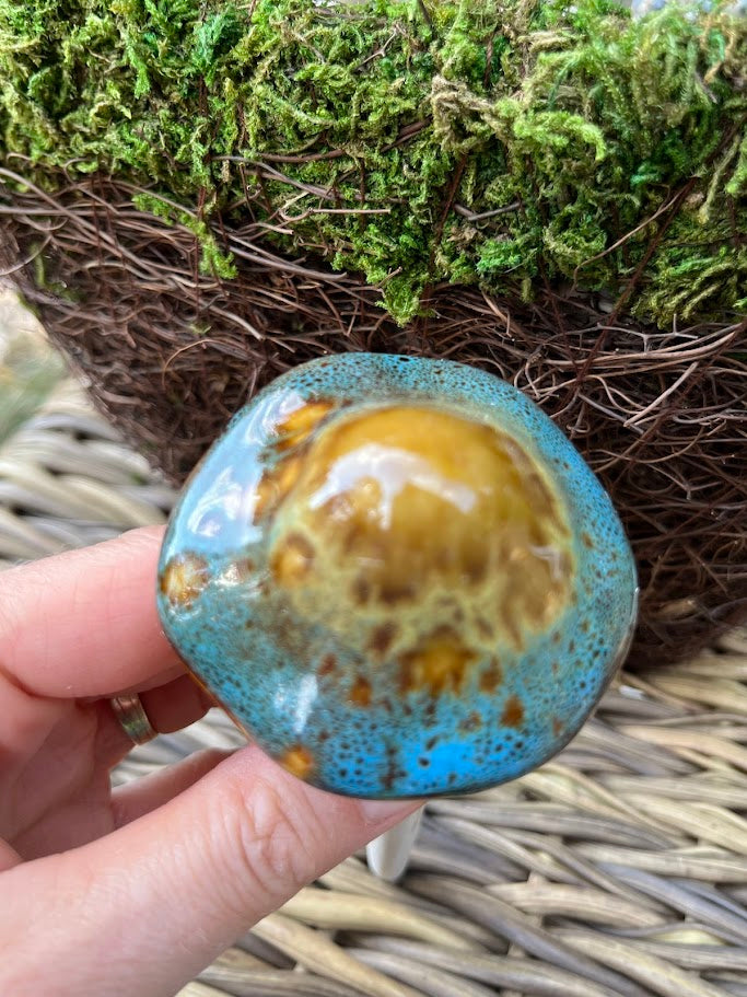 Hand holding a ceramic object with blue and brown glaze against a natural background