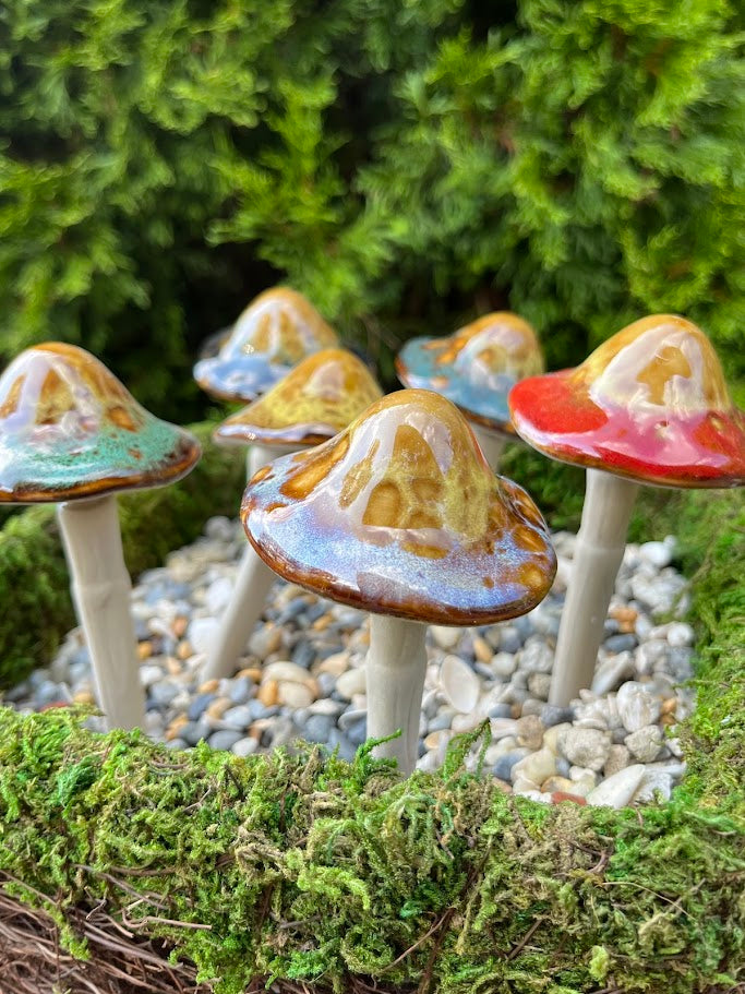 Colorful ceramic mushrooms on a natural background with greenery and pebbles.