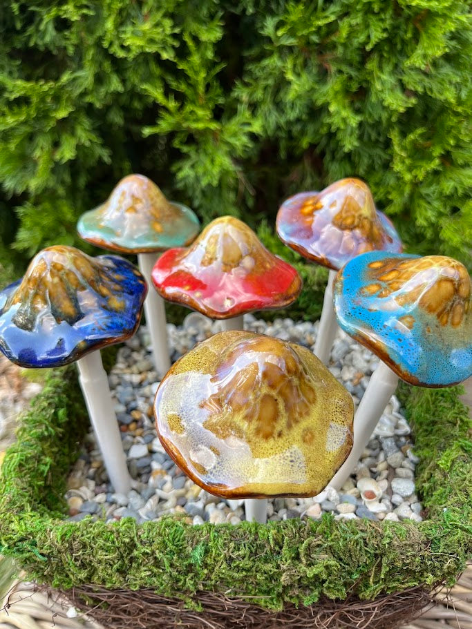 Colorful ceramic mushrooms on a bed of moss and small stones with greenery in the background.