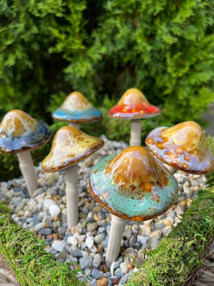 Decorative ceramic mushrooms on pebbles with greenery in the background