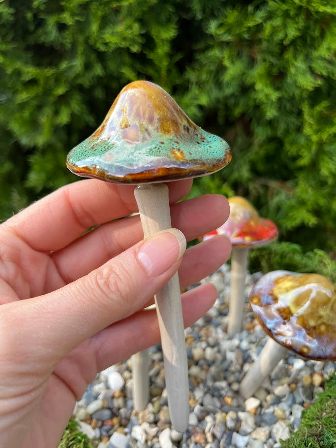 Hand holding a small mushroom-shaped object with a colorful cap against a natural background