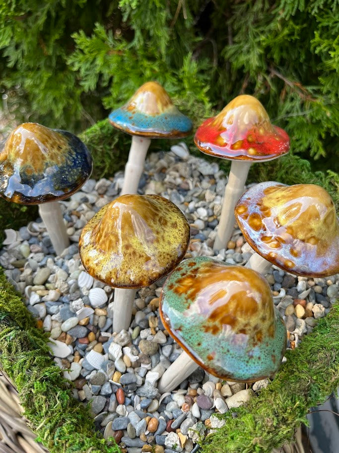 Set of ceramic mushrooms on a pebble and moss surface with greenery in the background