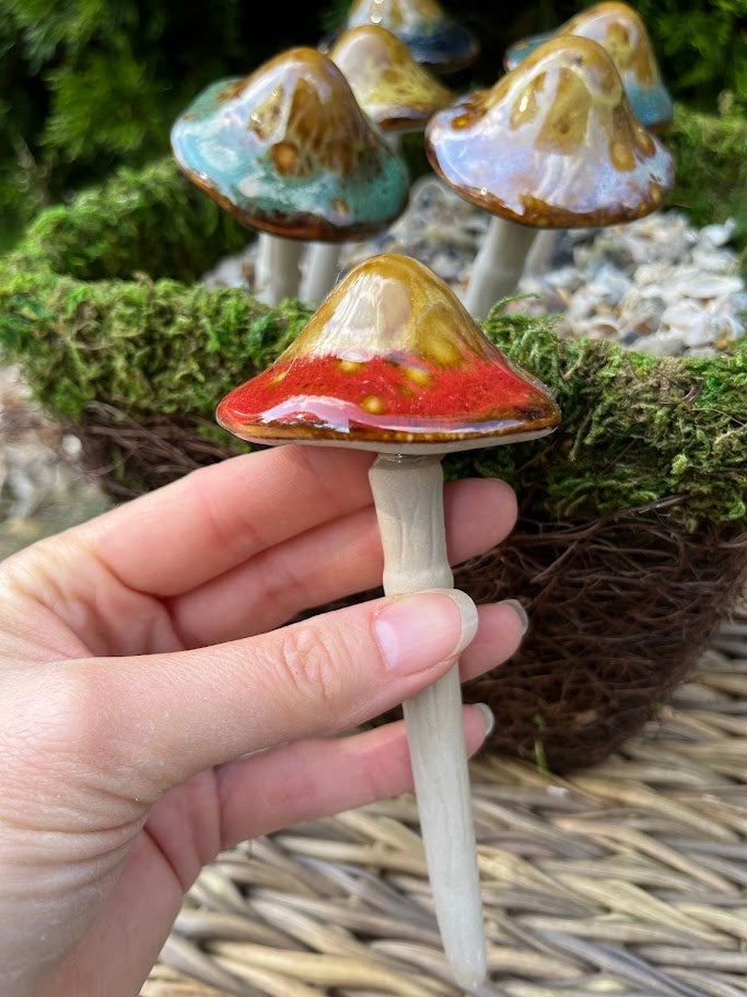 Hand holding a small ceramic mushroom with more mushrooms in the background