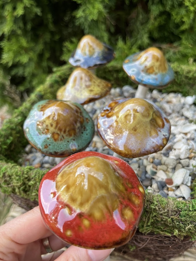Colorful ceramic mushrooms with a hand holding one against a natural background.