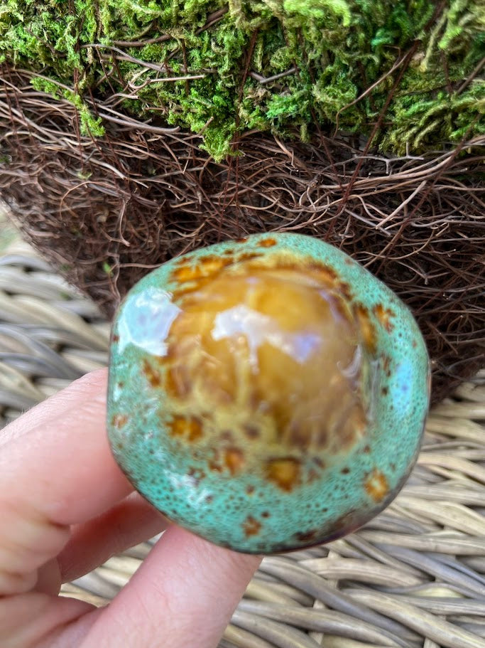Turquoise stone with brown patterns held by a hand against a natural background