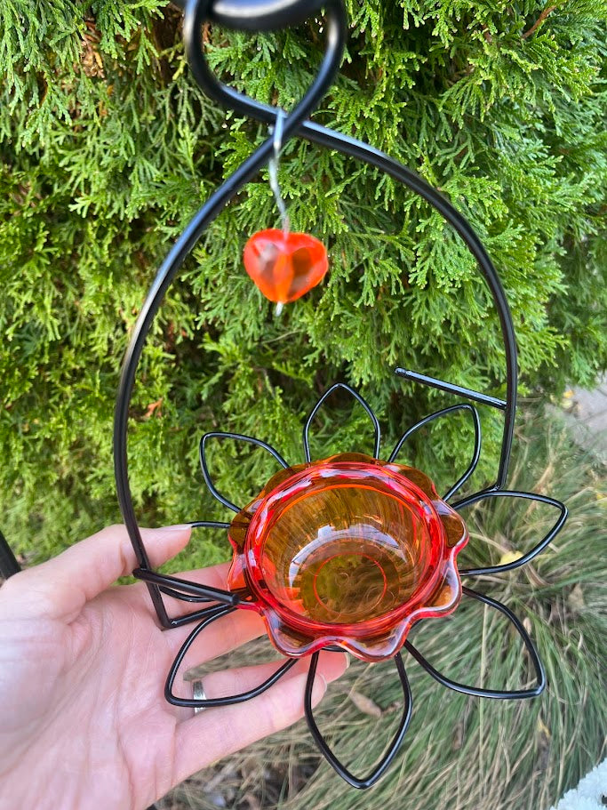 Hanging orange oriole bird feeder with black metal stand against a green foliage background