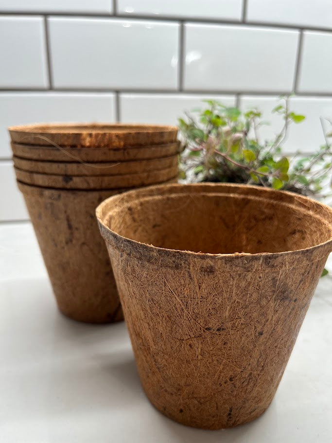 Stack of brown biodegradable pots on a white surface with a tiled wall background.