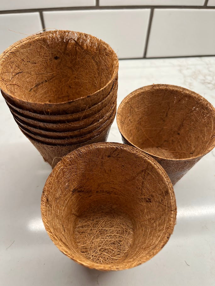 Stack of brown coir pots on a white surface with tiled background