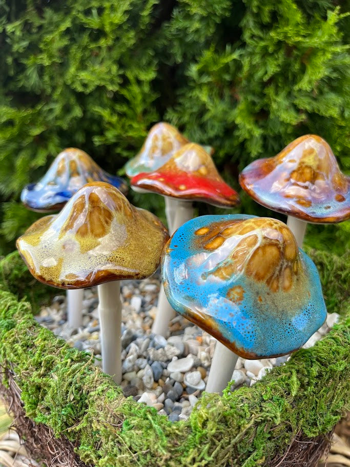 Colorful ceramic mushrooms on a bed of moss and small stones with greenery in the background.