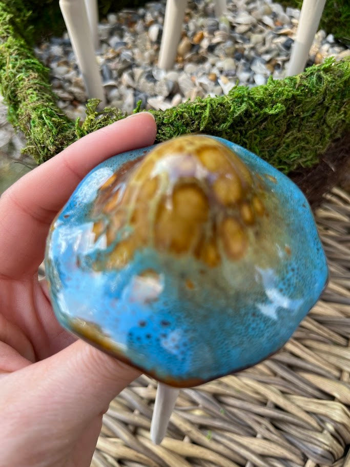 Hand holding a blue and brown ceramic object with a natural background