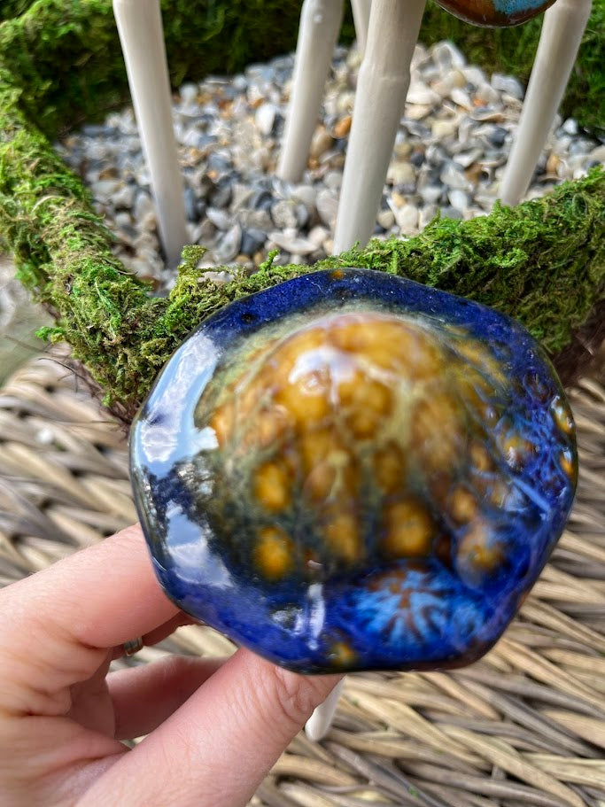 Hand holding a blue and yellow glass bead with a natural background