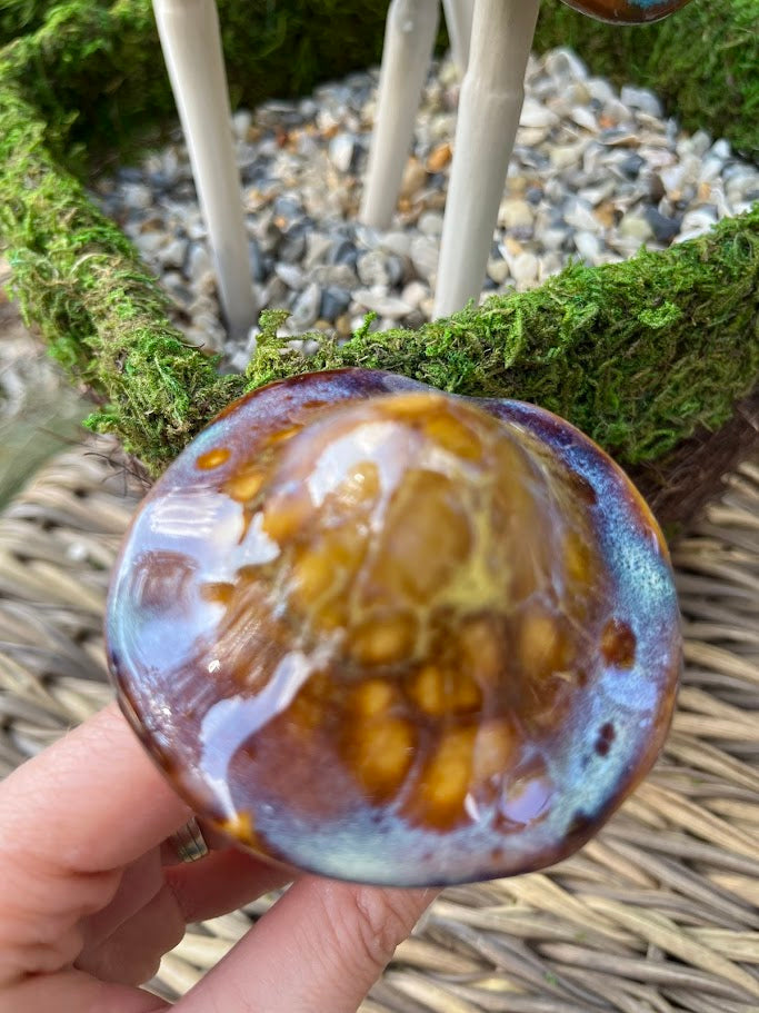 Close-up of a hand holding a textured, multicolored object against a natural background with moss and stones.