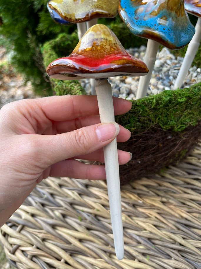 Hand holding a ceramic mushroom with a colorful cap against a natural background