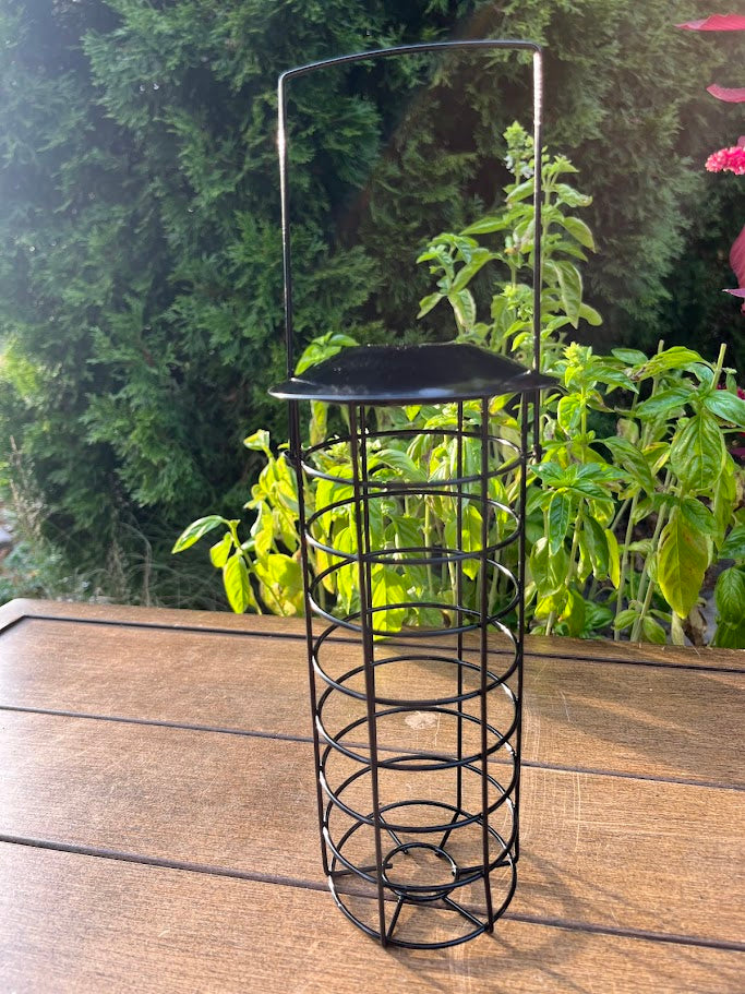Black metal bird feeder on a wooden surface with greenery in the background
