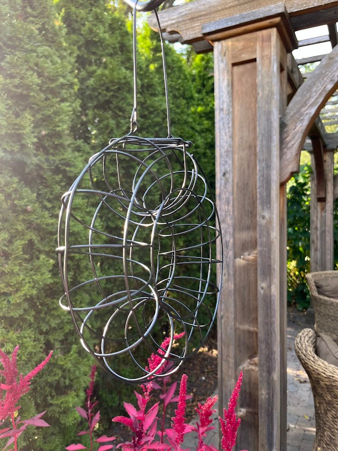 Decorative metal spiral hanging outdoors with greenery and wooden structure in the background