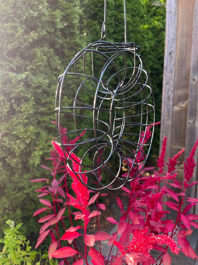 Decorative metal hanging sculpture with red foliage in a garden setting