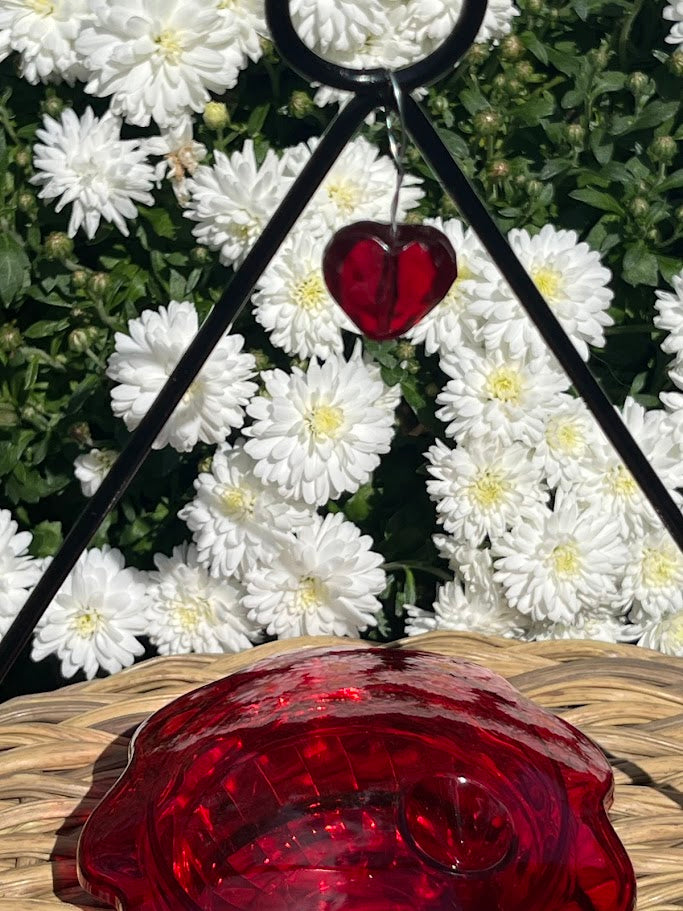Red glass heart ornament on a stand with white flowers in the background
