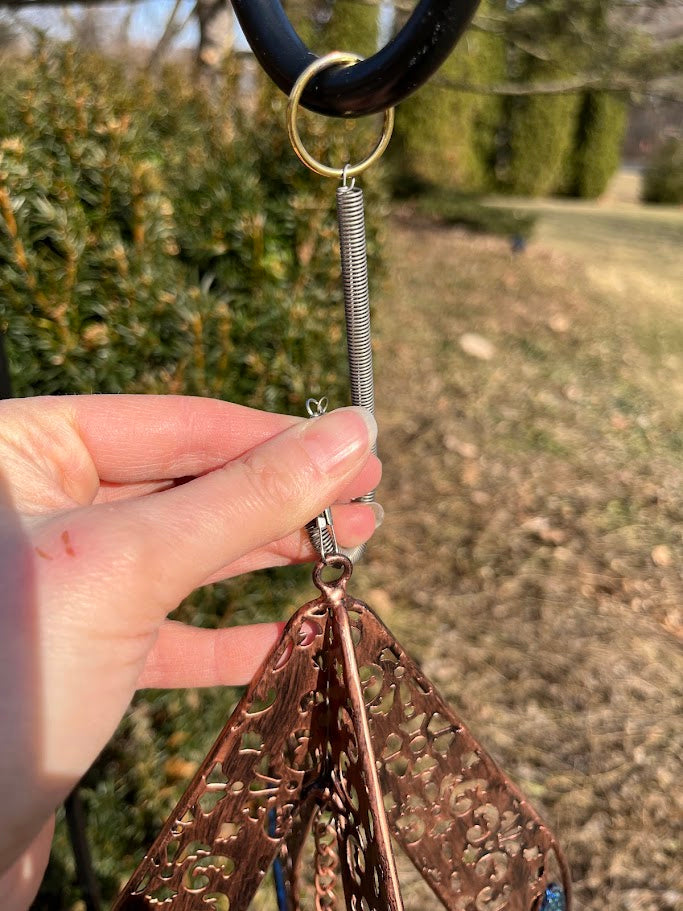 Hand holding a decorative spring with intricate design against a blurred outdoor background