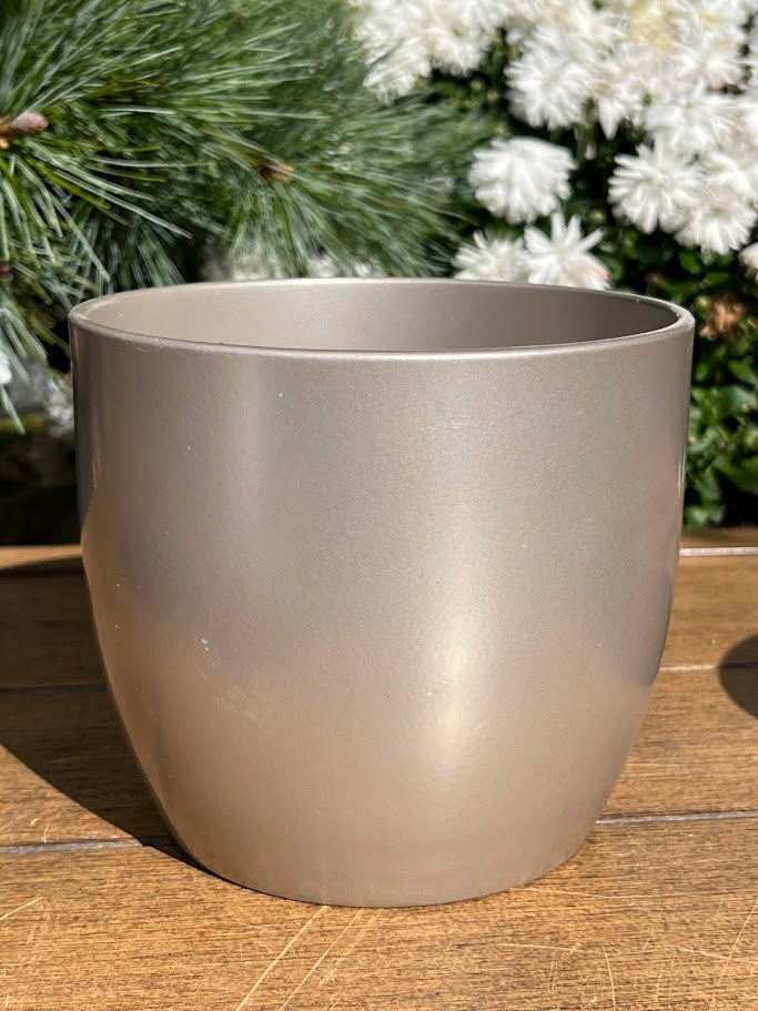 Beige pot on a wooden surface with greenery and white flowers in the background