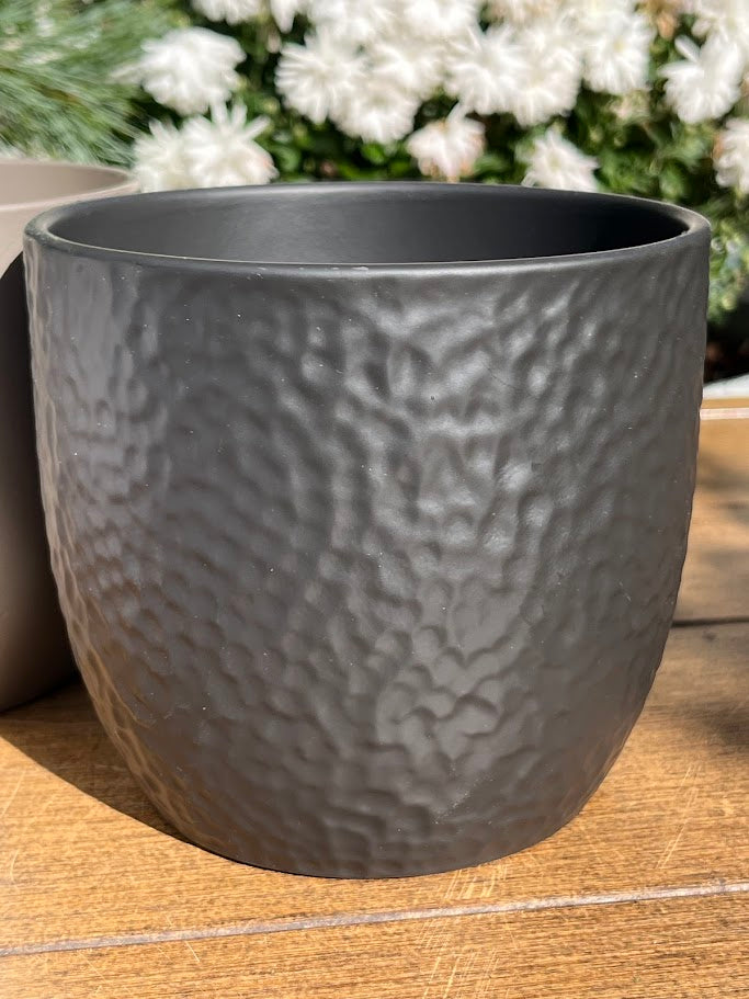 Gray textured pot on a wooden surface with blurred white flowers in the background
